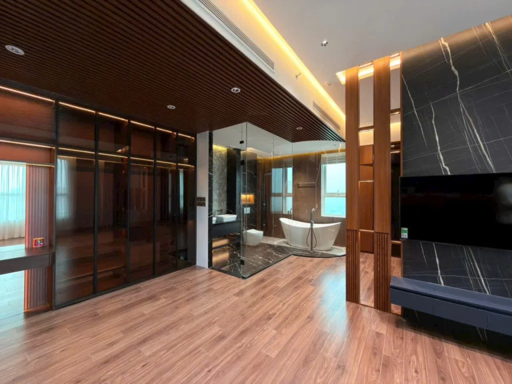 Nội thất bên trong Penthouse Duplex Sadora 9 (Thiết kế nội thất phòng ngủ master hiện đại với phòng tắm vách kính trong suốt, sàn gỗ, tủ áo cánh kính và tường ốp đá cẩm thạch tối màu, hình ảnh minh họa cho bài viết chia sẻ kinh nghiệm mua Sala.)